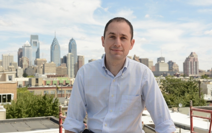 Ori Feibush sits on a rooftop with the Philadelphia skyline behind him.